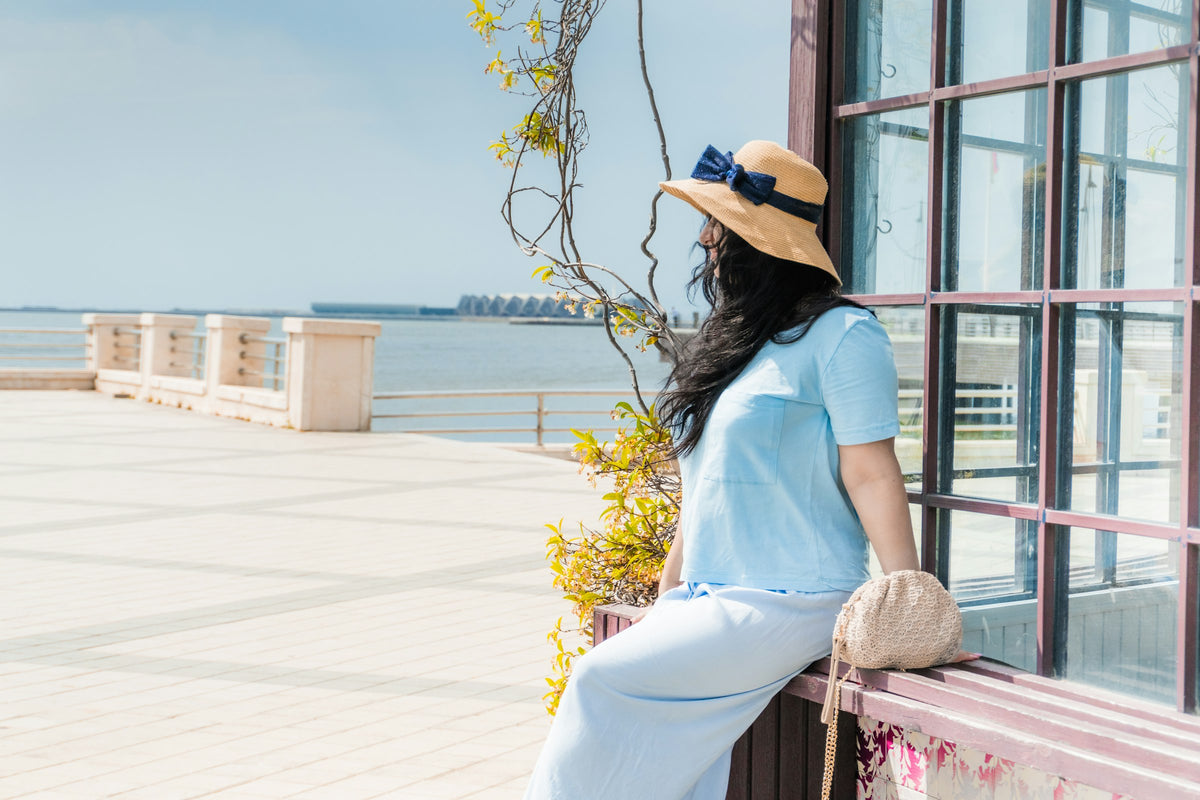 Woman in a straw hat with a navy bow sitting by the sea